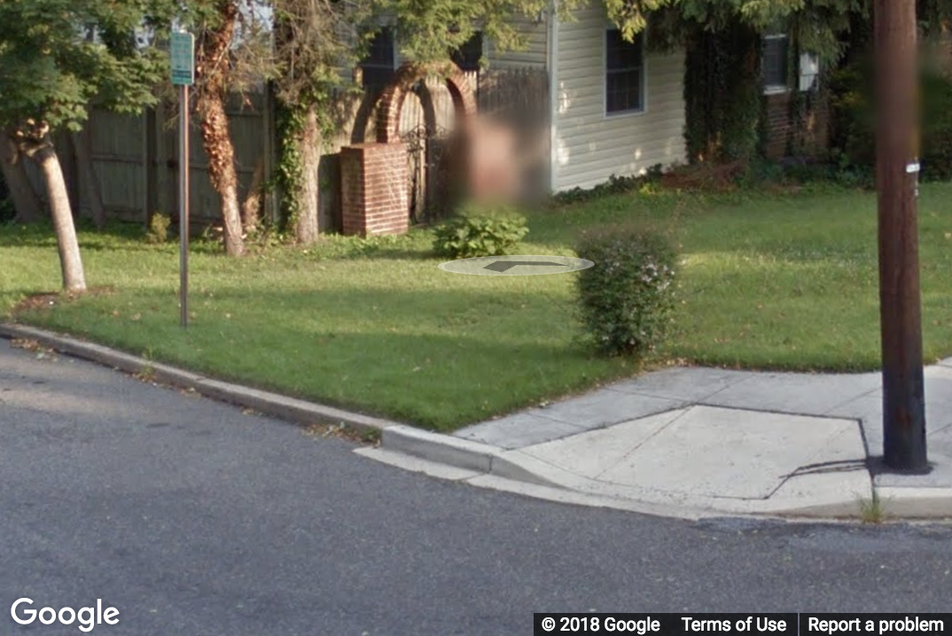 A Street View image of an intersection missing a sidewalk from one direction